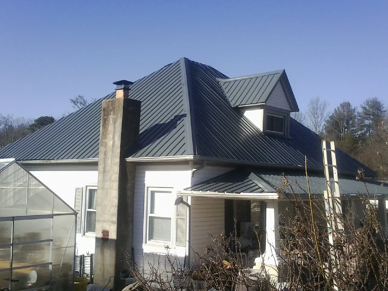 Dark blue standing seam metal roof on a white farmhouse with dormer — Slate & Tile Roof Repair by Roofing Brothers in Cresco