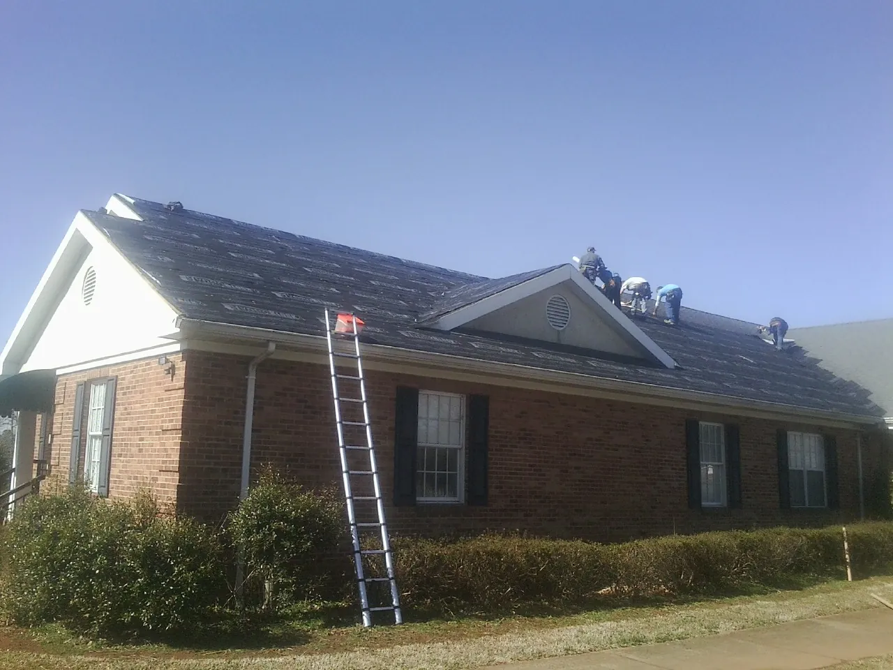 Crew tearing shingles off a brick ranch roof with a ladder set — Emergency Roof Repair work by our crew in Cresco