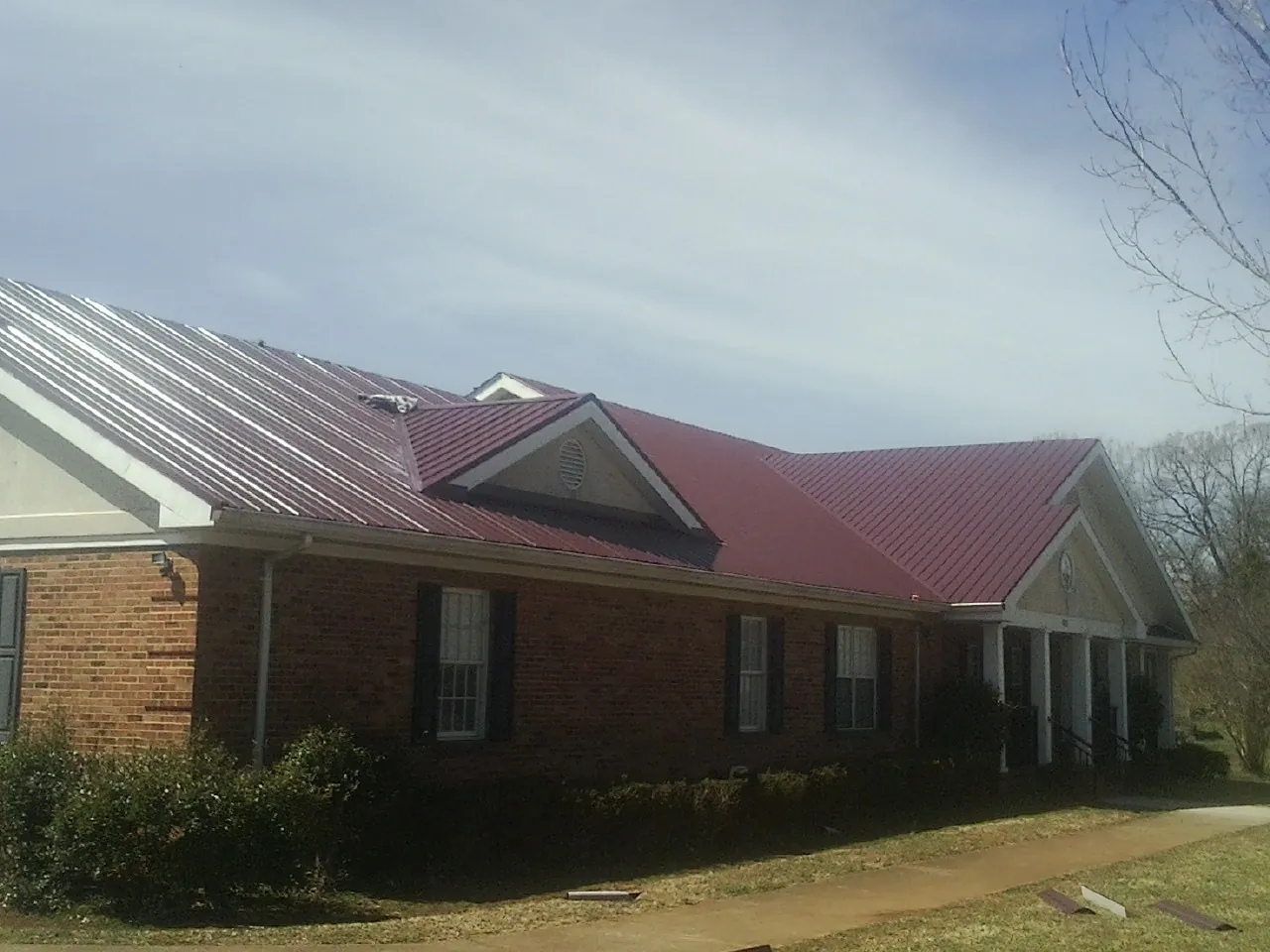 Red metal roof with gabled entries on a long brick building, from a Hail Damage Roof Repair job in Cresco