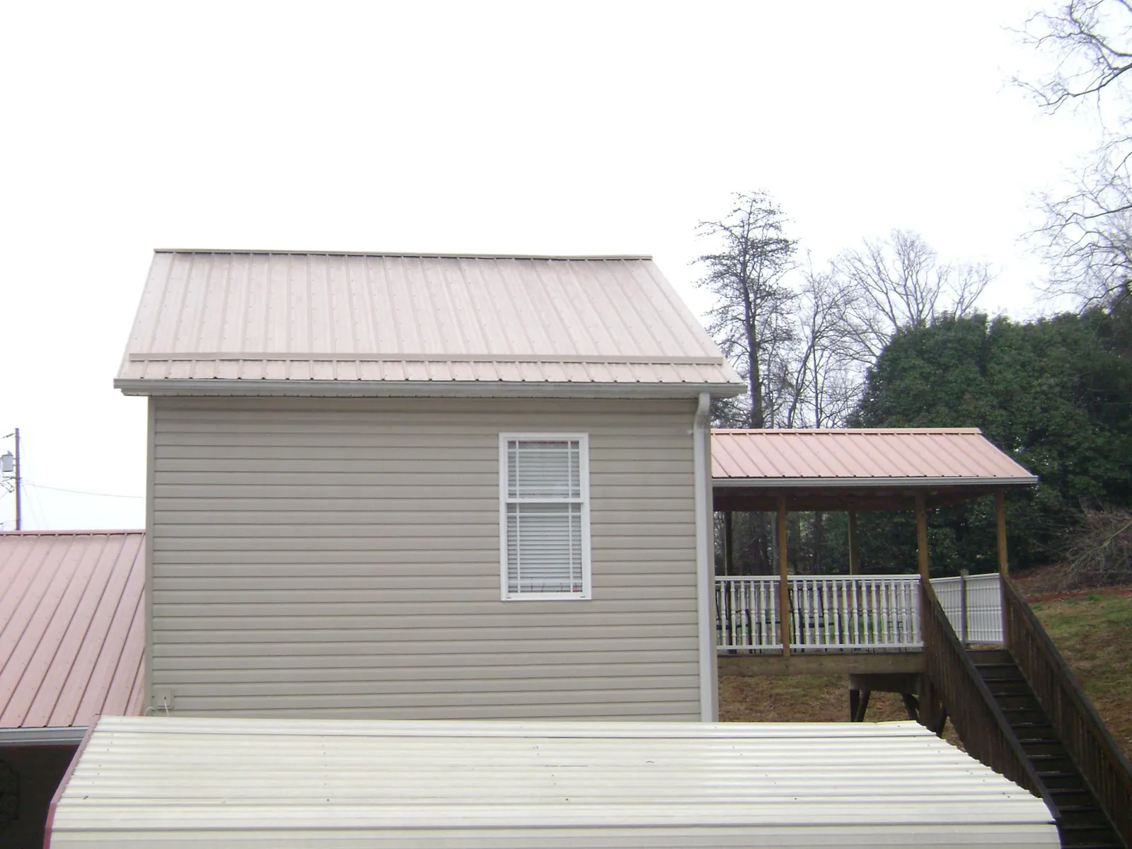 Tan metal roofs on a two story addition and attached porch, from a Roof Replacement job in Cresco